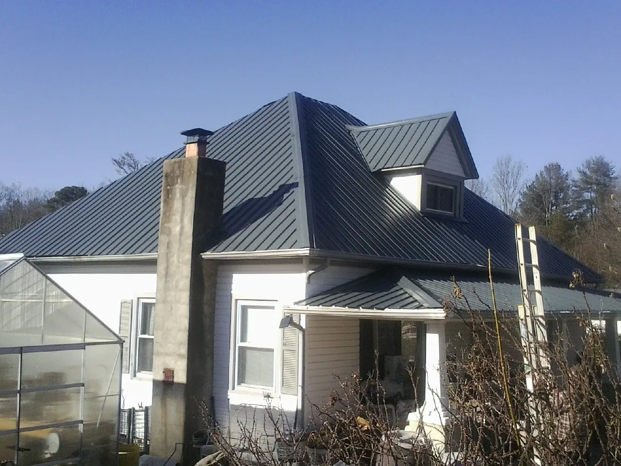 Dark blue standing seam metal roof on a white farmhouse with dormer — Slate & Tile Roof Repair by Roofing Brothers in Riceville