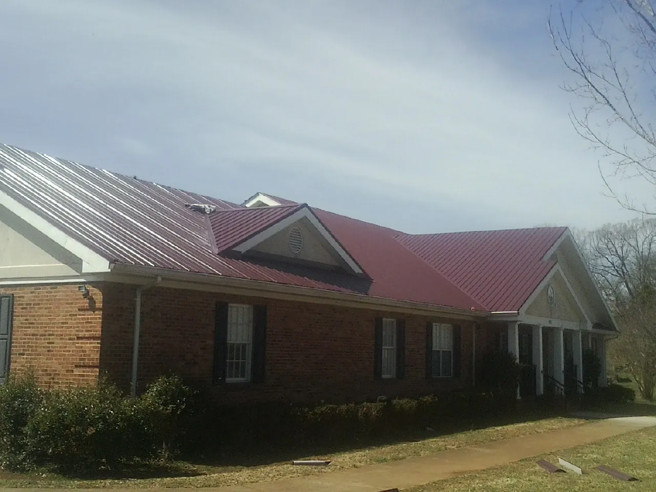 Red metal roof with gabled entries on a long brick building, from a Hail Damage Roof Repair job in Riceville