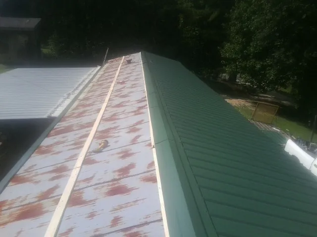 Old rusted panels beside newly installed green metal roofing — Wind Damage Roof Repair by Roofing Brothers in Riceville