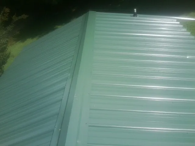 New green metal panels meeting at the ridge of a roof — Flat Roof Repair work by our crew in Riceville