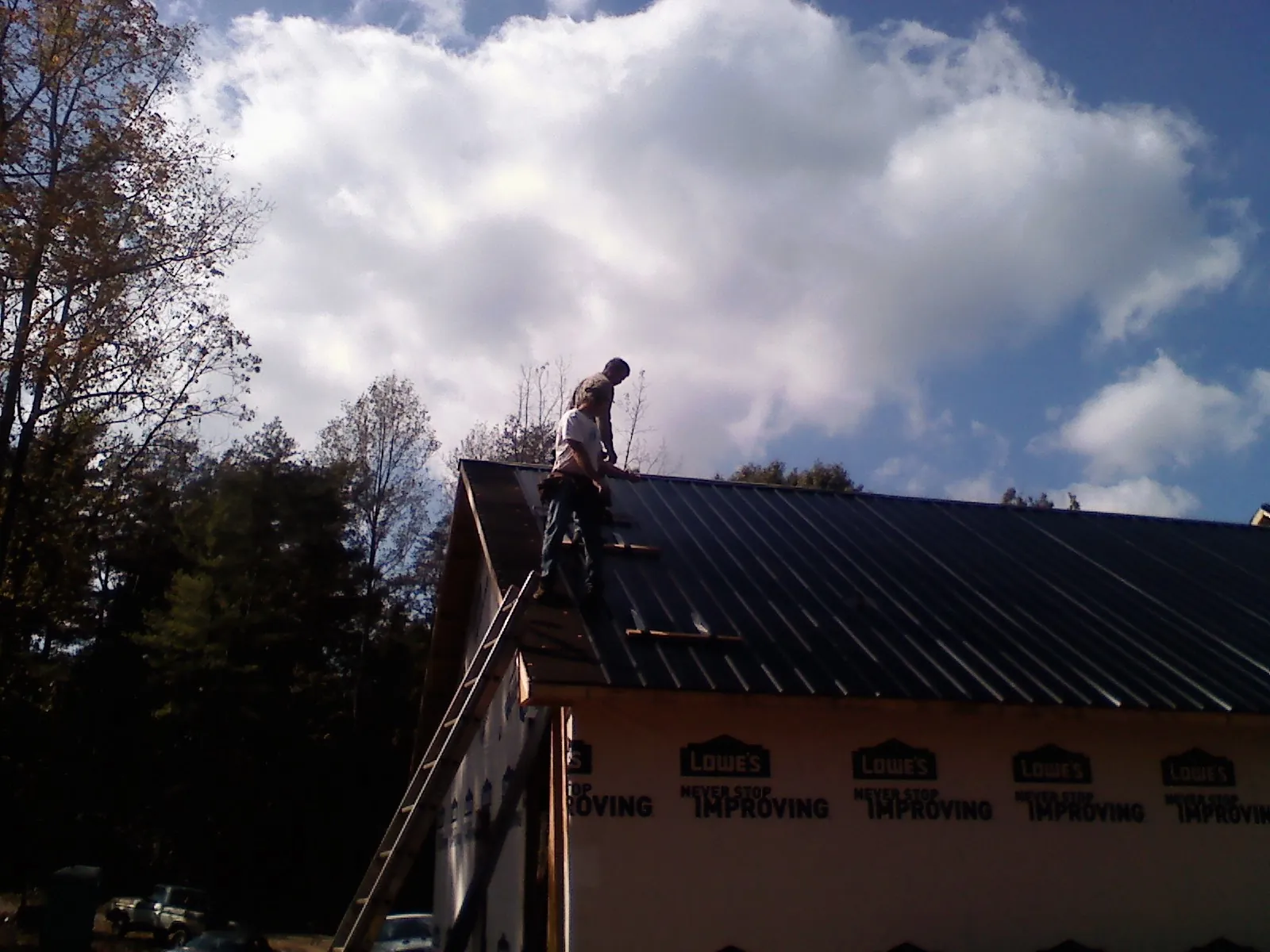 Roofer fastening dark metal panels high against a cloudy sky, from a Roof Inspection job in Riceville