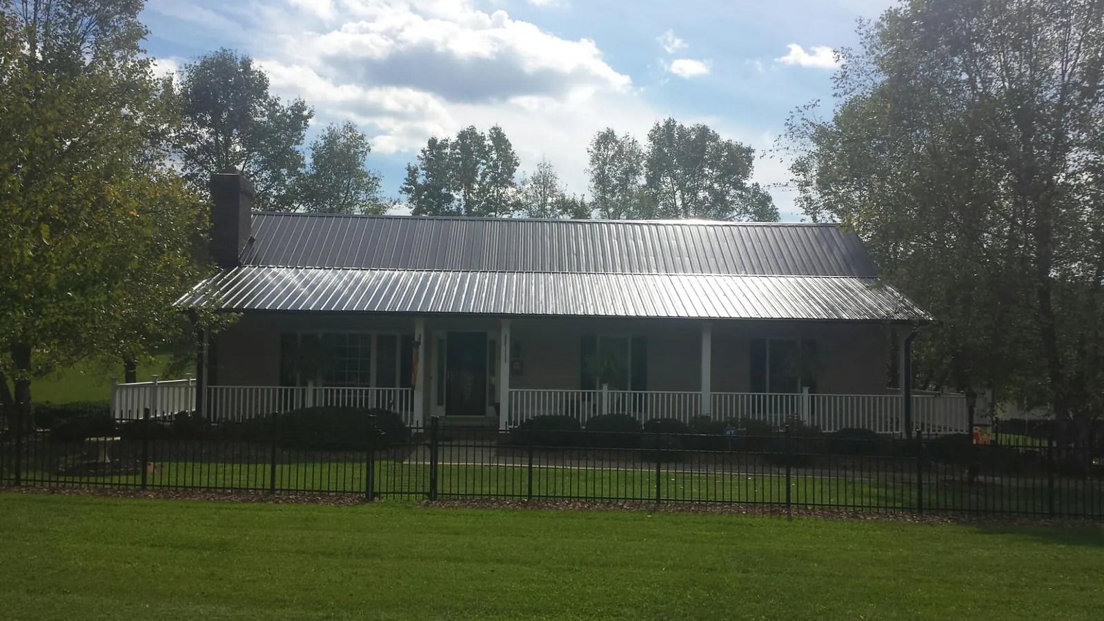 Gray metal roof on a brick ranch with a full width front porch — Gutter Guard Installation work by our crew in Riceville