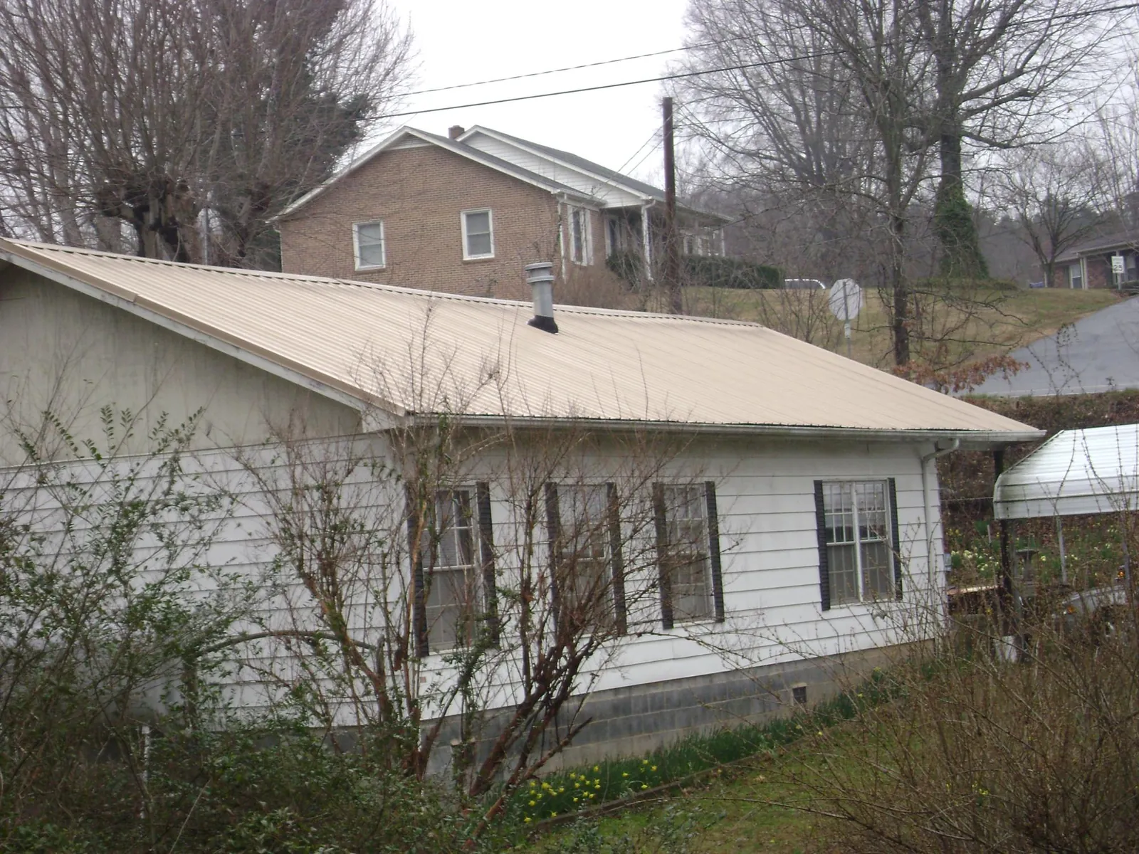 Tan metal roof on a white sided house set into a hillside — Commercial Roofing by Roofing Brothers in Riceville